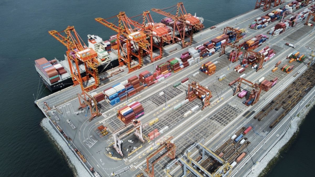 Vista aérea de terminal portuário com navio, guindastes e contêineres.